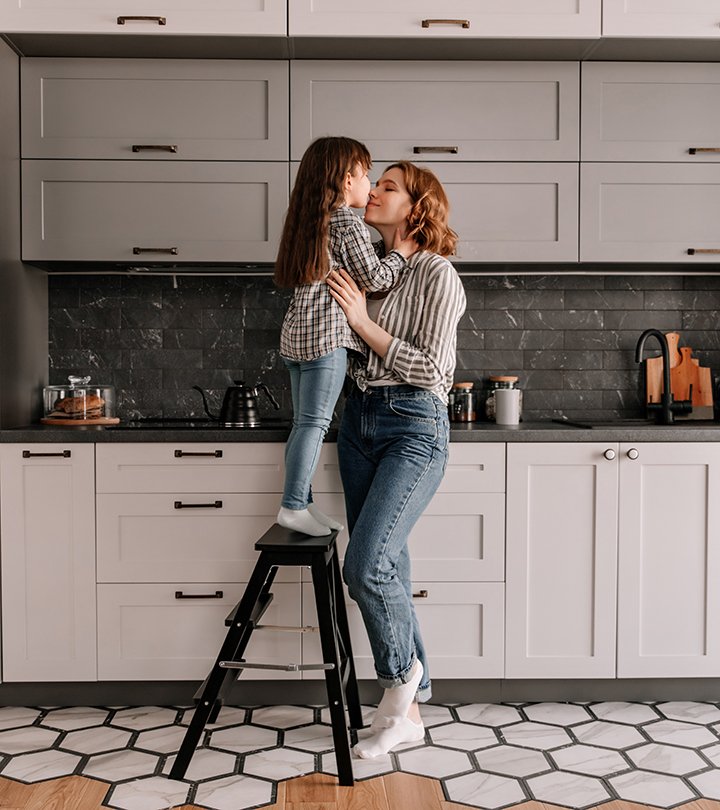 Portrait of little girl stands on stairs and hugs mother in kitchen